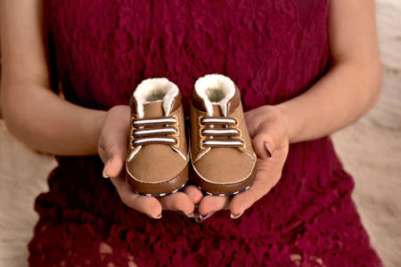 Pregnant woman holding baby shoes in her hands at Christmas time to announce that she is expecting a...