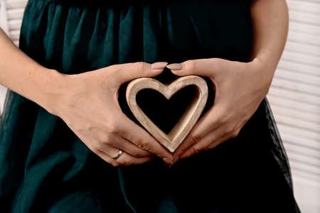 Pregnant woman holding a wooden heart in her hands and making love symbolの写真素材