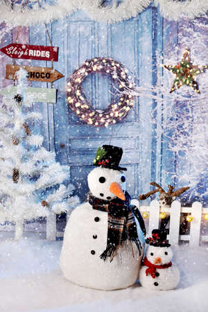 Winter scene with two snowman toys standing in front of house with blue doors and Christmas decorsの写真素材