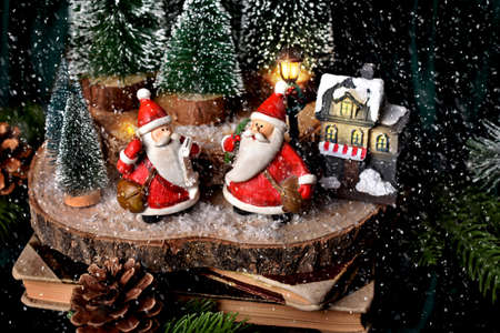Christmas decoration with winter scene on a slice of wood with two Santa Clauses, house and miniature Christmas trees and falling snowの写真素材