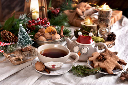 A cup of hot tea owl shaped tea pot and gingerbread cookies on Christmas table in rustic styleの写真素材