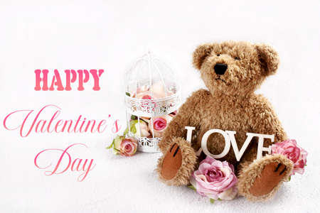 Valentines card with cute teddy bear with with roses and wooden LOVE inscription sitting on white background with empty copy space on leftの写真素材