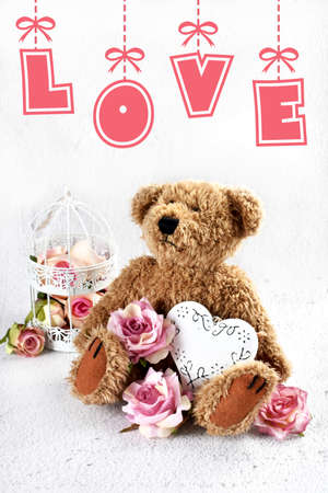 Valentines card with cute teddy bear with roses and a heart sitting on white background with copy space for own textの写真素材