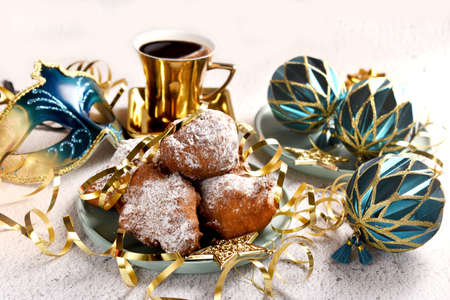 A plate of homemade donuts and a cup of coffee on carnival party table with venetian mask and ornaments in blue and golden colorsの写真素材