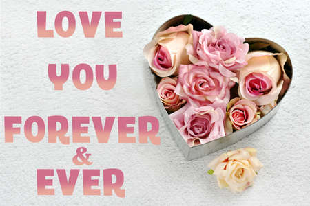 Valentines card with metal heart filled with pink rose flowers on a light concrete background with inscription Love you forever & everの写真素材