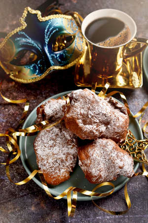 A plate of homemade donuts and a cup of coffee on carnival party table with venetian mask in blue and golden colorsの写真素材