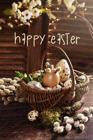 Easter still life with wicker basket filled with eggs and catkins on wooden table in rustic styleの写真素材