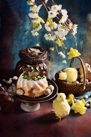 Easter ring cake and wicker basket with chickens and flowers on grunge backgroundの写真素材
