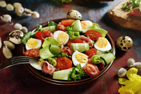 A plate with fresh Easter salad with prosciutto ham, quail eggs, cherry tomatoes, cucumber, avocado and lettuce on grunge backgroundの写真素材