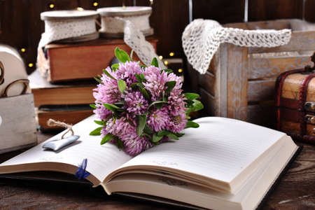 Small bunch of pink clover flowers on opened planner lying on rustic style tableの写真素材