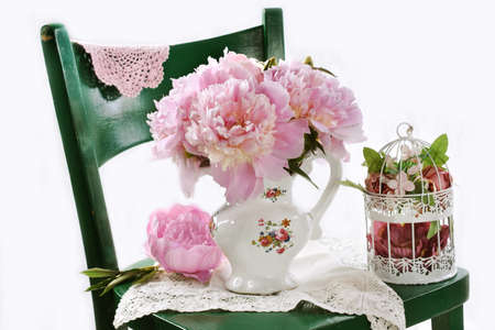 Bouquet of pink peonies in porcelain vase standing on green wooden chairの写真素材