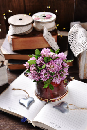 bunch of pink clover flowers in clay vase on opened book in rustic styleの写真素材