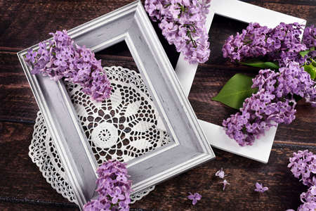 Dark wooden background with two frames, lace napkin and fresh purple lilac blossomsの写真素材