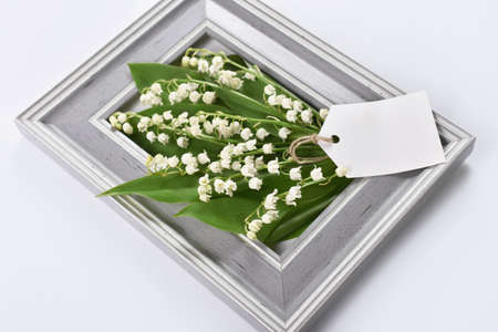 Gray frame and bunch of lilies of the valley with paper tag for own text on white backgroundの写真素材