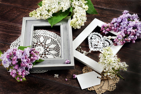 Dark wooden background with two frames, lace napkins and fresh purple and white lilac blossoms