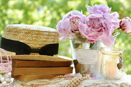 Romantic style still life with pink fresh peonies, straw hat and old books on the table in the gardenの写真素材