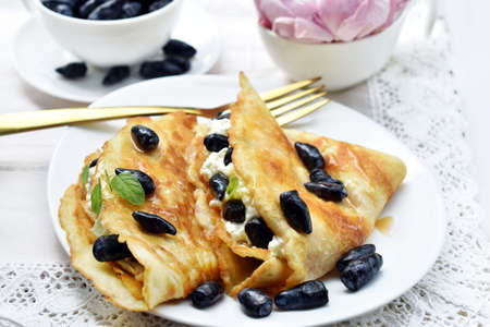 Homemade pancakes with cottage cheese, cream and honeysuckle berries on white plate