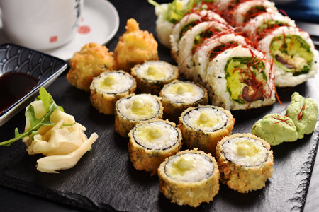 Japanese sushi set with panko fried rolls and vegan rolls with shiitake mushroom and vegetables and green tea on black boardの写真素材