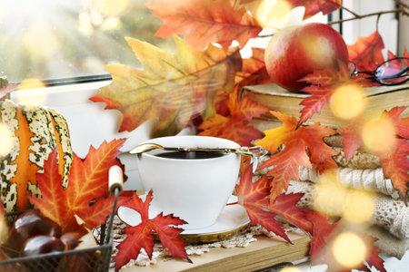 Autumn cup of coffee on the windowsill with colorful maple leaves decoration
