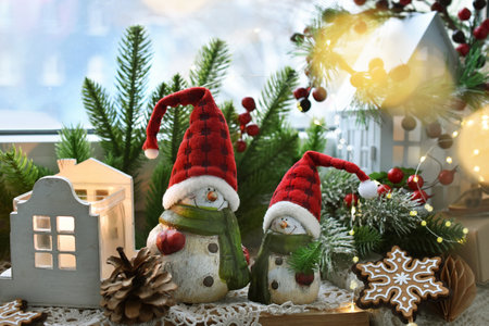 Two snowman figurines in Santa Claus caps, candles and Christmas decors standing on a windowsillの写真素材