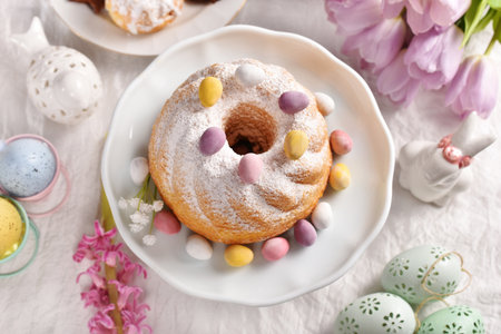Top view of traditional Easter ring cake sprinkled with powdered sugar and candy eggs on festive...