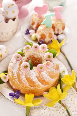 Easter table with homemade ring cake sprinkled with powdered sugar and muffins with sugar decors in pastel colorsの写真素材