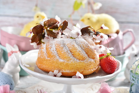 Easter table with homemade ring cake sprinkled with powdered sugar, spring decorations in pastel colorsの写真素材