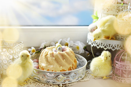 Easter ring cake with icing , chickens and seasonal decors on windowsill in sunny day