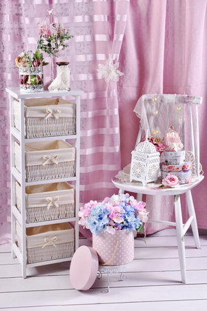 Vintage style interior with white shelves with wicker baskets and old chair with decors and flowers with pink curtainsの写真素材