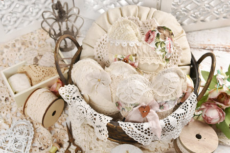 Vintage style still life with a basket filled with handmade hearts and a pillow sewn of linen and laces on a white wooden tableの写真素材