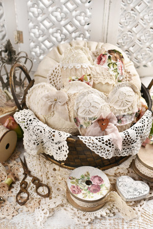 Vintage style still life with a basket filled with handmade hearts and a pillow sewn of linen and laces on a white wooden tableの写真素材