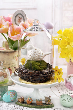 Easter table in vintage style with white ceramic bird in a nest under glass cloche, decors and flowersの写真素材