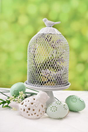 Easter decoration with wire bird cage, ceramic bird and eggs on the table in the gardenの写真素材
