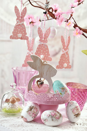 Easter table arrangement with colorful eggs and wooden bunny decor and pink paper bunnies hanging on a twigの写真素材