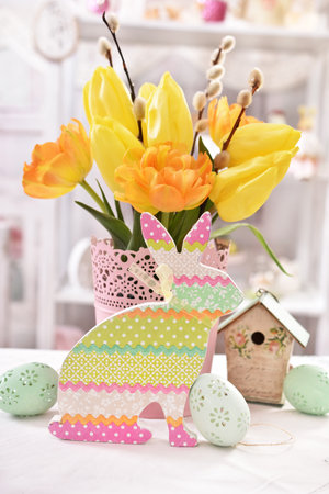 Easter table decoration with colorful bunny decor, eggs and bunch of yellow tulips in vaseの写真素材