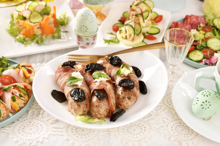 Easter white sausage wrapped in bacon with prune and horseradish, stuffed eggs and salads on festive tableの写真素材