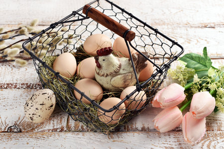 Vintage style Easter wire basket with eggs and hen figurine on white wooden tableの写真素材