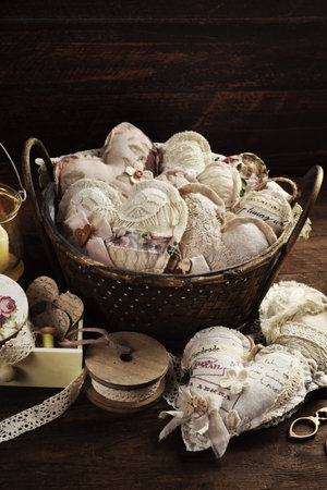 Handmade fabric and lace hearts in vintage style in wicker basket on wooden tableの写真素材