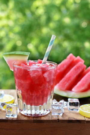 A glass of watermelon drink with ice cubes and fresh fruit on the table in summer gardenの写真素材