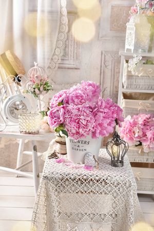 Shabby chic style interior with a bunch of fresh pink peonies on a small coffee table with a lace tableclothの写真素材