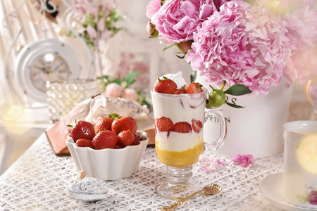 Strawberry and cream dessert and fresh fruits on the table in vintage style with a bunch of pink peoniesの写真素材