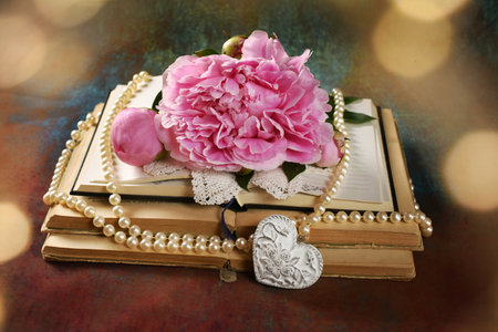 Vintage style arrangement with old opened books, pearls and pink peony flower on grunge background with lightsの写真素材