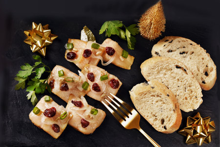 Top view of smoked herring fillets with cranberries and slices of bread on black slate boardの写真素材