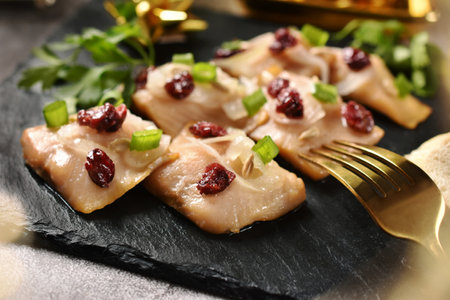 Christmas table with smoked herring fillets in oil with onion and dried cranberries on black slate board-closeupの写真素材
