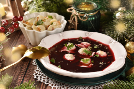 Traditional red borscht with dumplings filled with mushrooms and sauerkraut for Christmas Eve's supper on festive table in rustic styleの写真素材