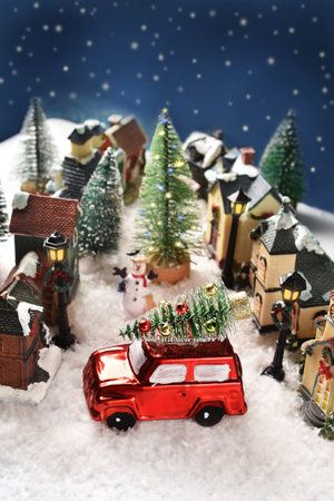 Winter scene miniature decoration with houses on the street in small town on Christmas night with a red car with Christmas tree on the roof -top viewの写真素材