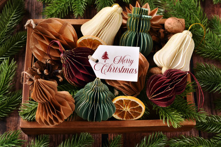 Top view of colorful handmade paper ornaments in various shapes and a label with Christmas greeting text in wooden box standing on the tableの写真素材
