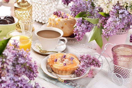 Sweet tartlet with pineapple and jelly and a cup of coffee on the table decorated with purple lilac blossomsの写真素材