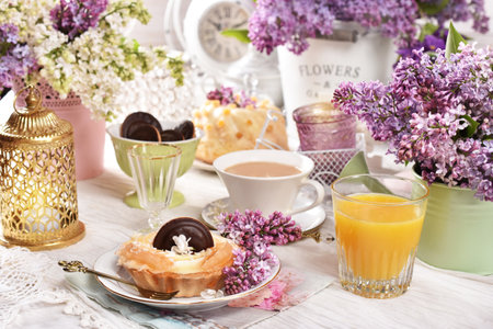Sweet tartlet with pineapple and jelly, orange juice and a cup of coffee on the table decorated with purple lilac blossomsの写真素材