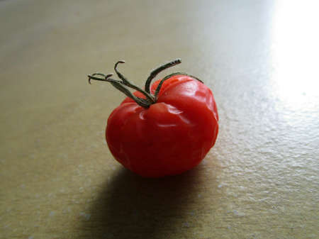 Macro detail of a ripe, red mini tomato on top of a table, lit with natural side light.の写真素材